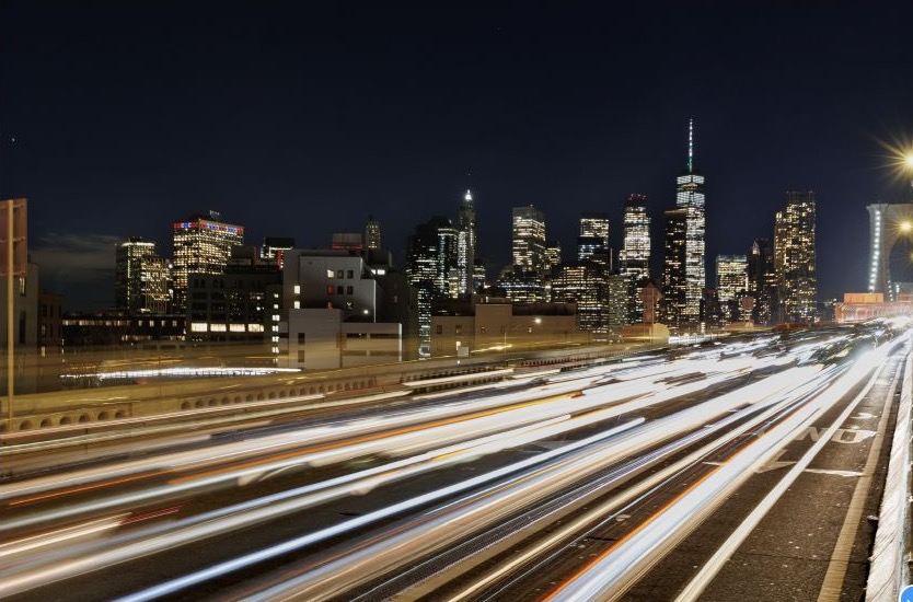 Avondbeeld van de skyline van New York met lichtsporen op de weg